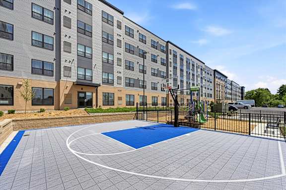 A basketball court is located in front of a multi-story apartment building.